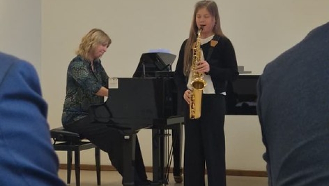 jauna saksofoniste uzstājas žūrijas priekšā, aiz viņas pie flīģeļa spēlē pianiste