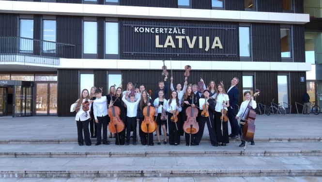 Stīgu kamerorķestris ar diriģentu nostājušies priekšā koncertzālei ,,Latvija’’