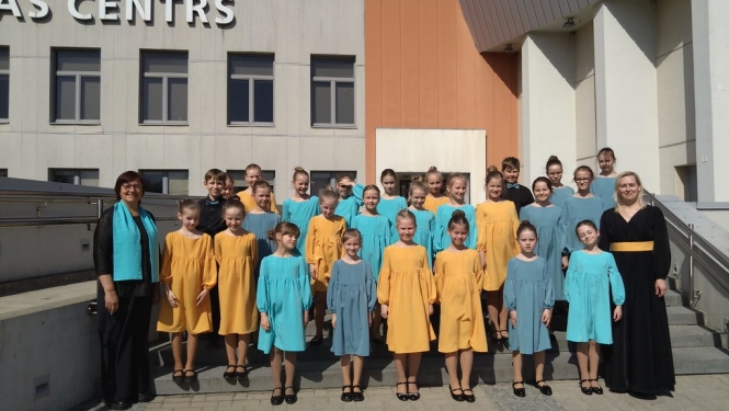bērnu koris ar divām skolotājām saulainā dienā nostājušies uz kāpnēm