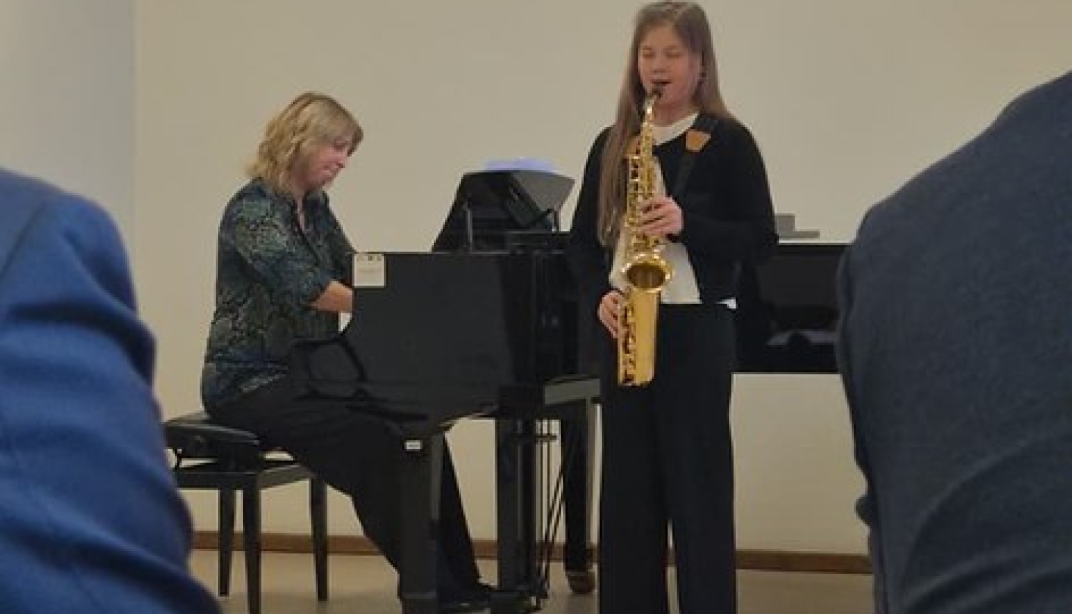 jauna saksofoniste uzstājas žūrijas priekšā, aiz viņas pie flīģeļa spēlē pianiste